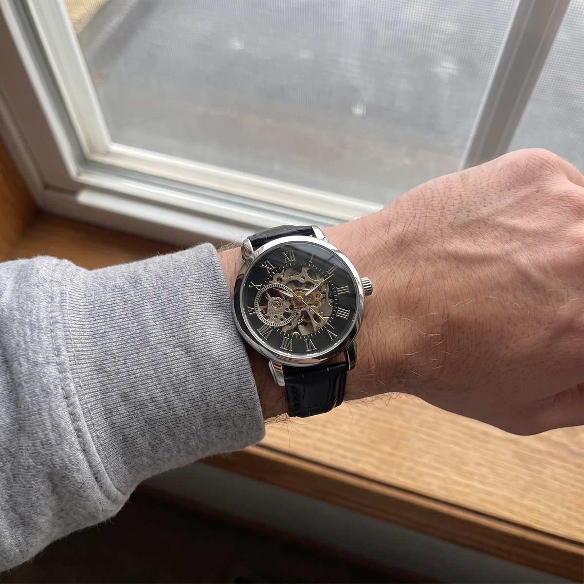 The watch worn on a wrist by a window, skeleton dial and gears visible